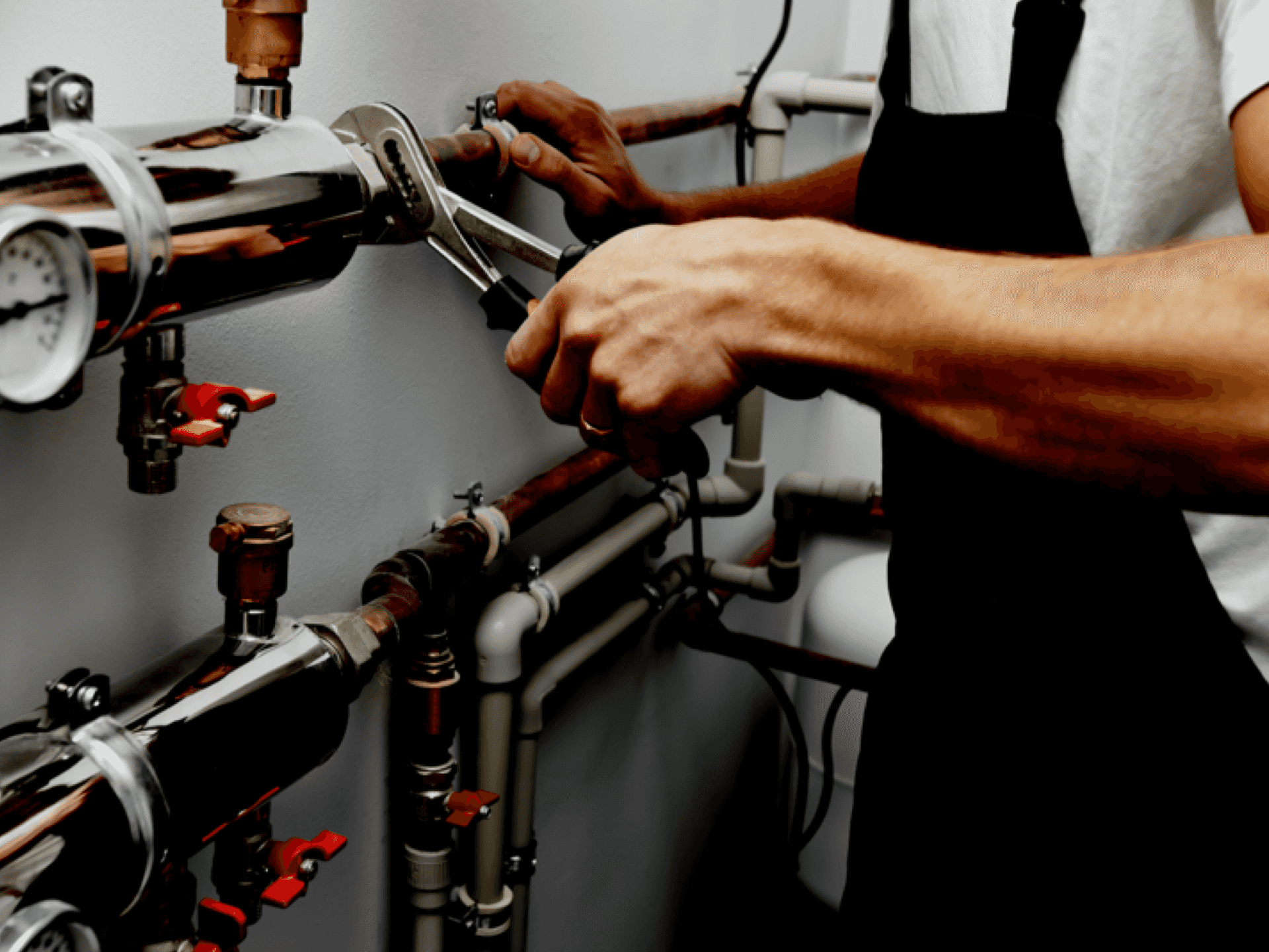 Ein Klempner in einer Schürze arbeitet in einem gut ausgestatteten Maschinenraum an der Einstellung komplexer Rohrverbindungen mit Schraubenschlüsseln.