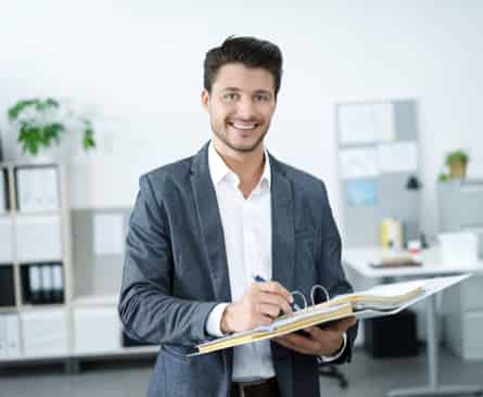 Ein lächelnder Geschäftsmann hält einen offenen Ordner in einem modernen Büroumfeld.