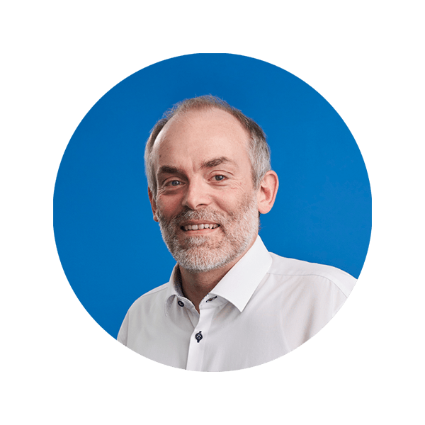 Lächelnder Mann mittleren Alters mit hellem Bart und weißem Hemd vor blauem Hintergrund.