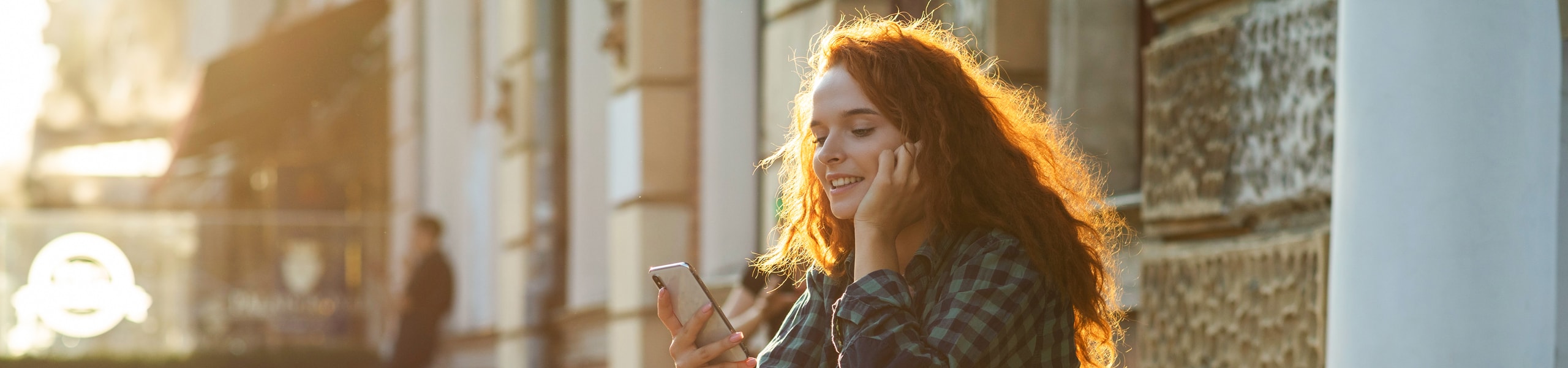 Frau sitzt bei Sonnenuntergang auf den Stufen und schaut fragend auf ihr Smartphone