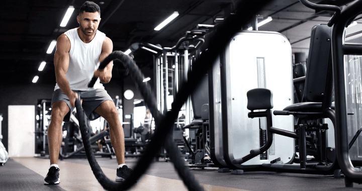 Ein Mann trainiert mit Battle Ropes in einem mit verschiedenen Trainingsgeräten ausgestatteten Fitnessstudio.
