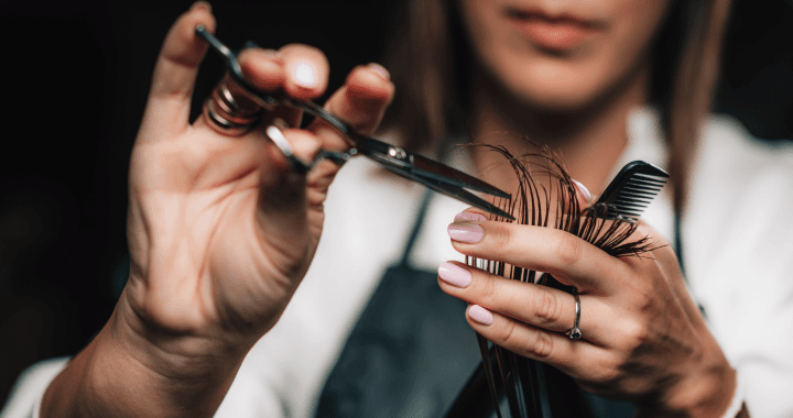 Eine Nahaufnahme einer Friseurin, die mit einer Schere Haare schneidet und einen Kamm hält, wobei der Fokus auf ihren Händen und Werkzeugen liegt.