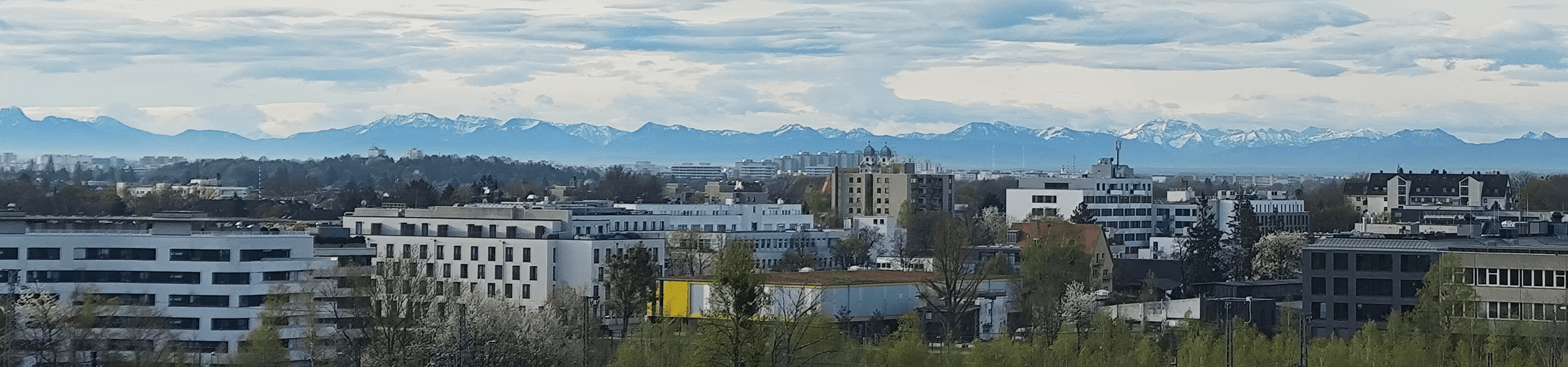 Ein Panoramablick auf die Skyline von München mit schneebedeckten Bergen in der Ferne.