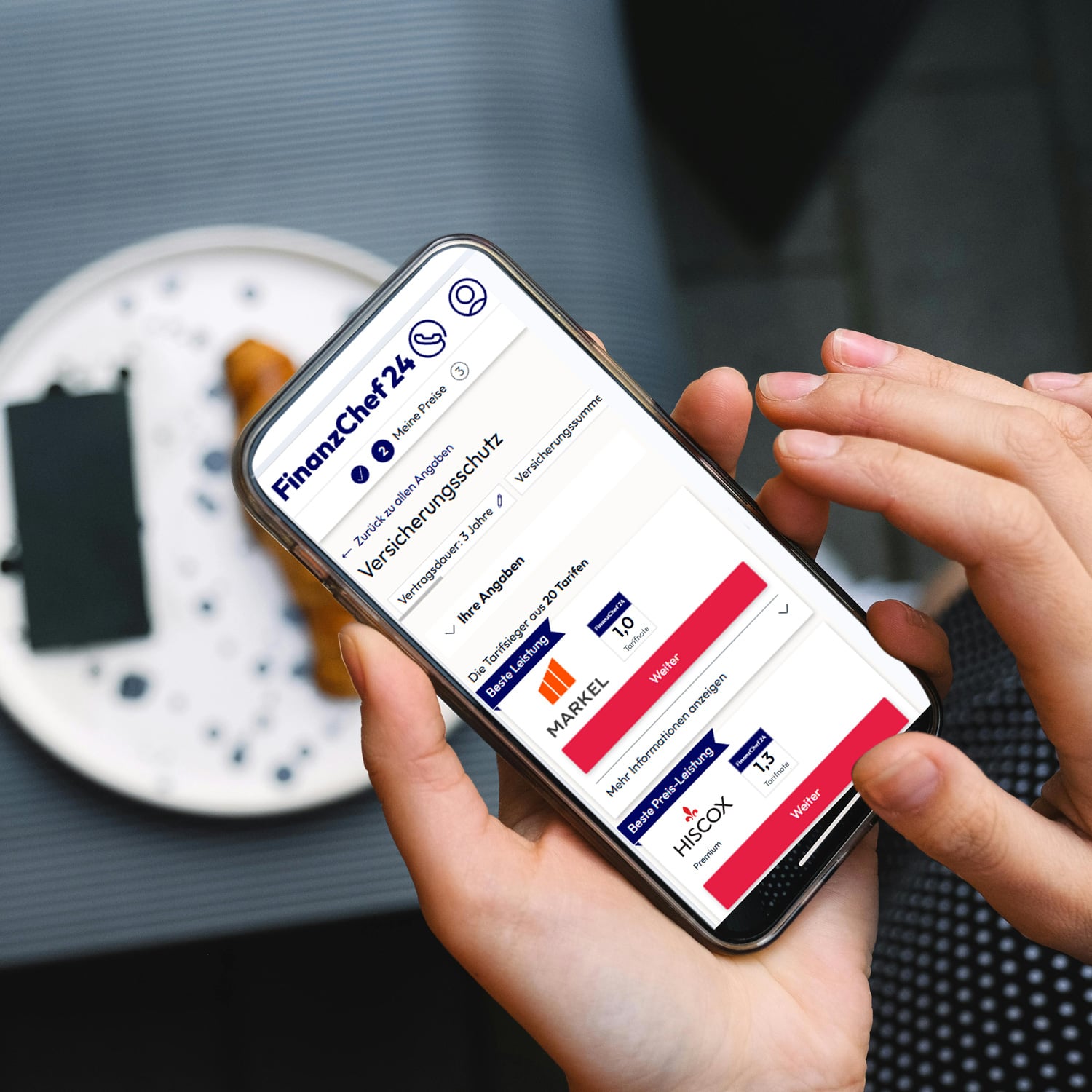 Mobiltelefon mit Cyber-Versicherungsvergleich vor einem Teller mit Croissant